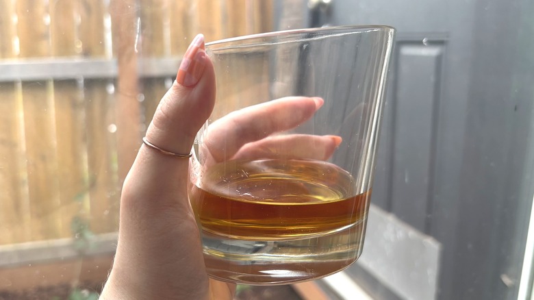 Hand holding glass of Buchanan's Green Seal whisky in front of window