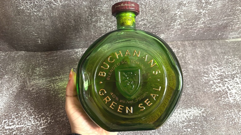 Hand holding green bottle of Buchanan's Green Seal on black background