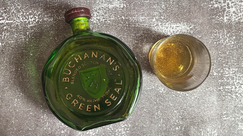 Green bottle of Buchanan's Green Seal next to glass of whisky on black background
