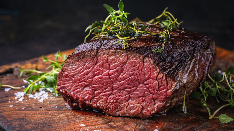 The Denver cut steak that has been nicely seared on the outside, pink inside, on a wooden cutting board with salt and herbs scattered about.