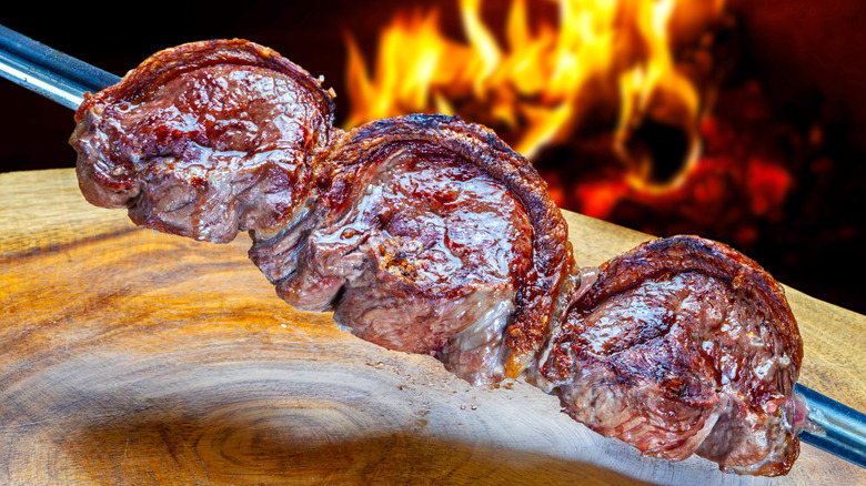 Fire grilled picanha steaks on a sword above a wooden cutting board.