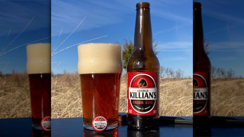 a bottle of George killian's next to a pint glass with the beer and a foamy head, with a field and trees in the background