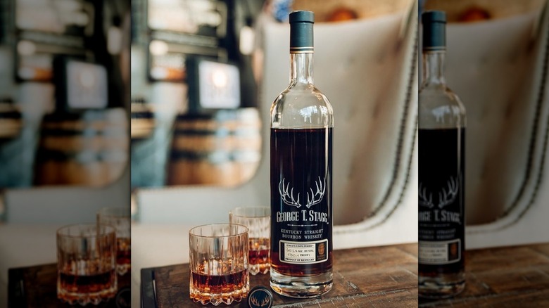 Bottle of George T. Stagg whiskey next to two rocks glasses of whiskey on wooden table
