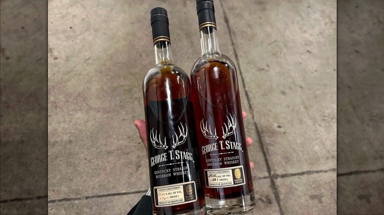 Hand holding two bottles of Buffalo Trace George T. Stagg above sidewalk