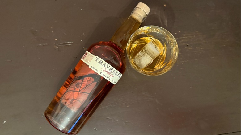aerial view of Traveller Whiskey laying on its side with a glass of it poured on the rocks