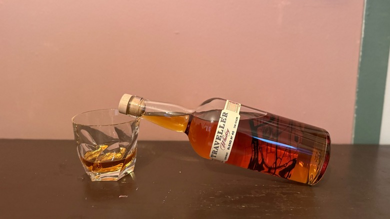 Glass of neat whiskey with Traveller Whiskey bottle laying on its side