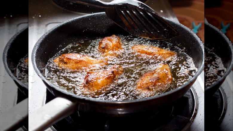 five chicken wings frying in fat in a pan
