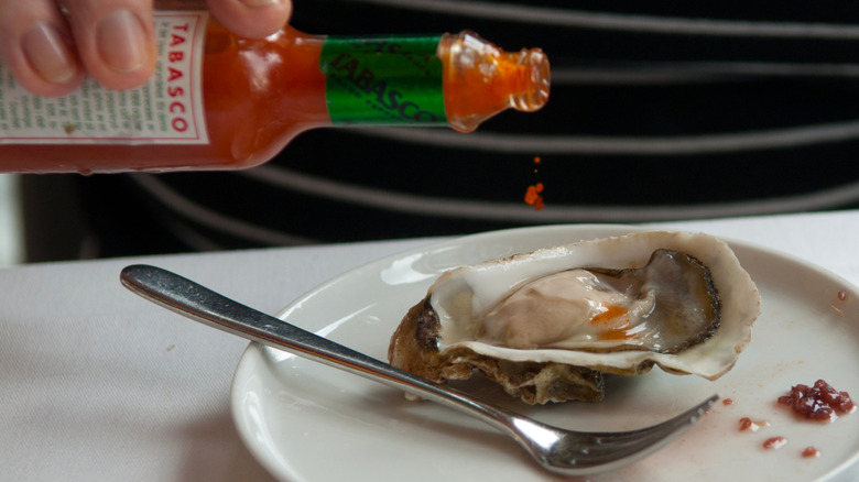 Person dropping Tabasco onto a raw oyster