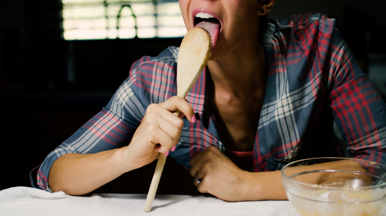 Woman licking wooden spoon in kitchen