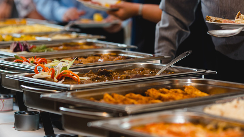 Buffet food service at event banquet, stainless steel catering trays with assorted hot dishes, people serving themselves