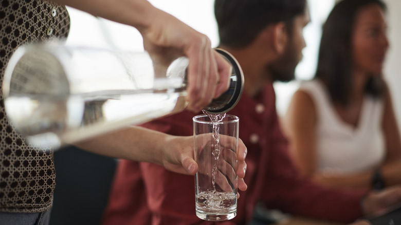 Close up of server pouring water into glass at restaurant
