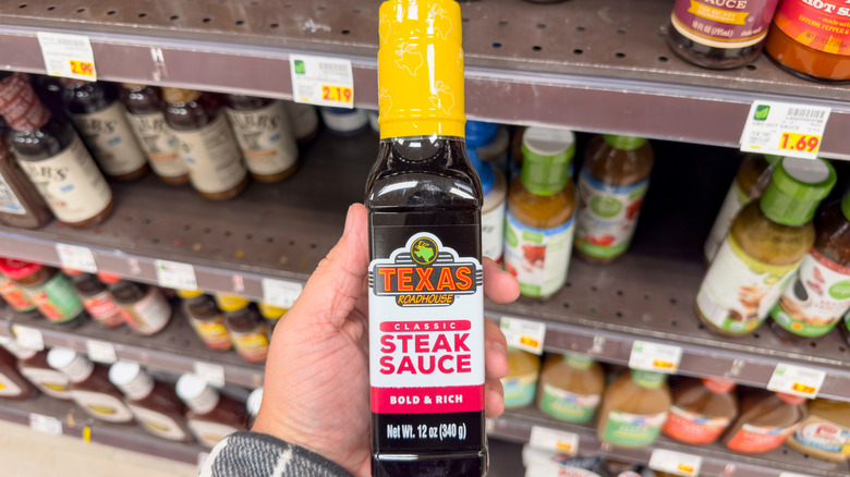 A hand holding Texas Roadhouse Classic Steak Sauce in a store, at the sauce aisle