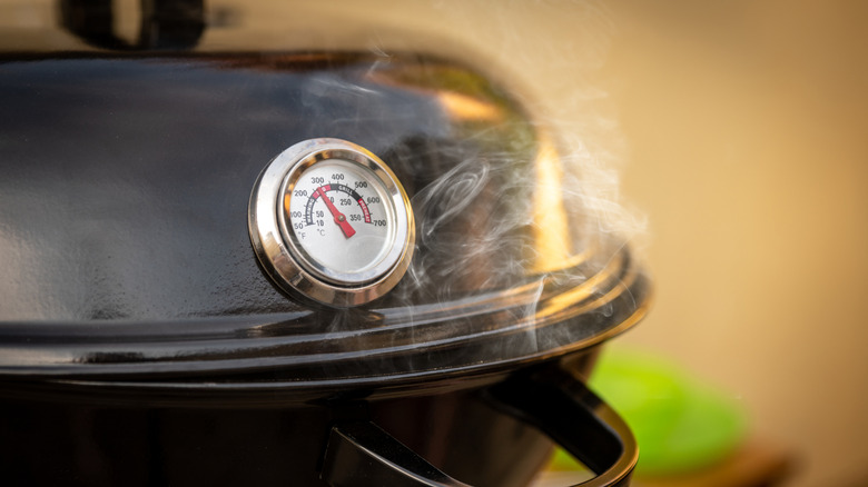 A thermometer resting on a smoking charcoal barbecue grill