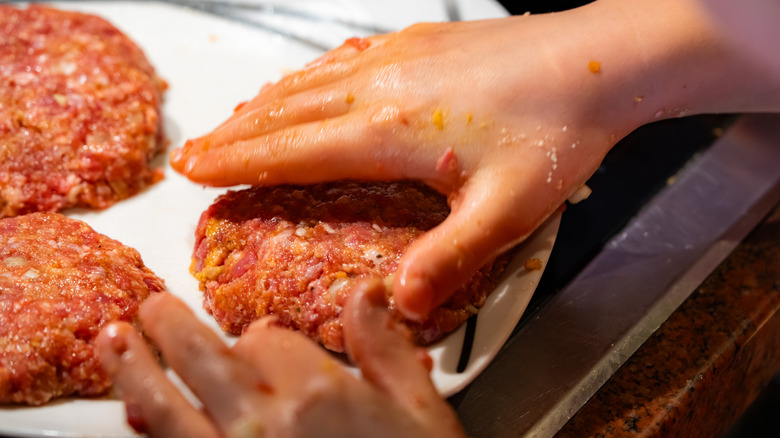 A close-up of a hand forming a burger patty on parchment paper
