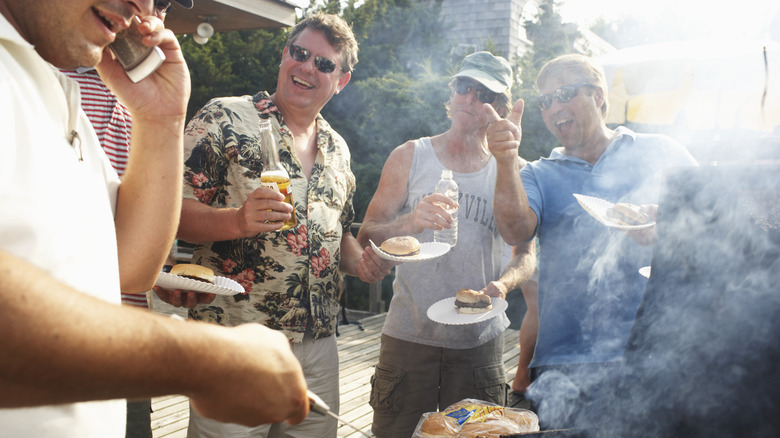 A gaggle of grill dads hanging out around a barbecue grill