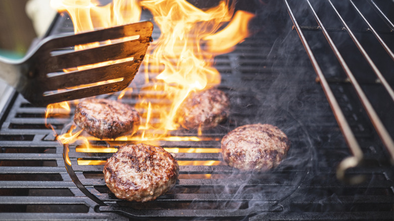 Burgers on a grill with cast-iron grates with flames roaring beneth them