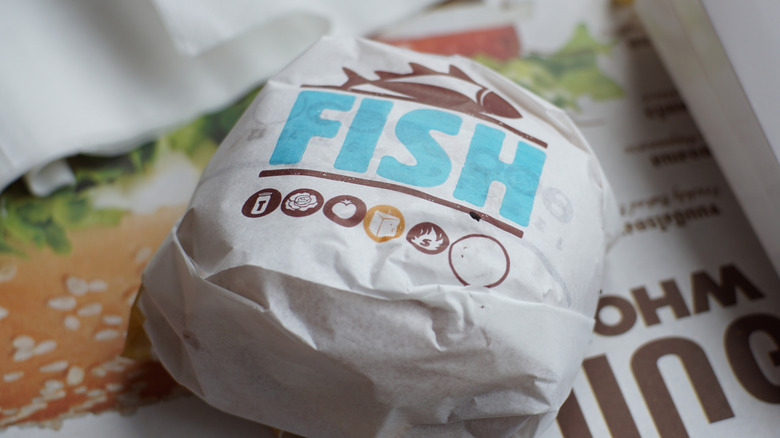 A wrapped up Burger King fish sandwich on a tray with a container of fries.