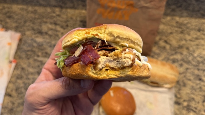 hand holding Burger King's bacon Swiss Royal chicken sandwich with bite taken