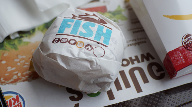 A Burger King fish sandwich in its wrapper on a tray.