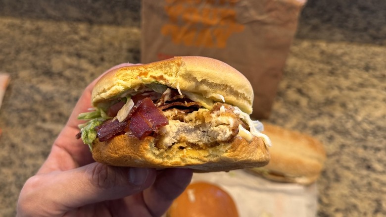 hand holding Burger King's bacon Swiss Royal chicken sandwich with bite taken