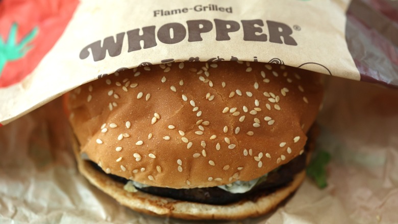 A Burger King Whopper half covered by its paper wrapper
