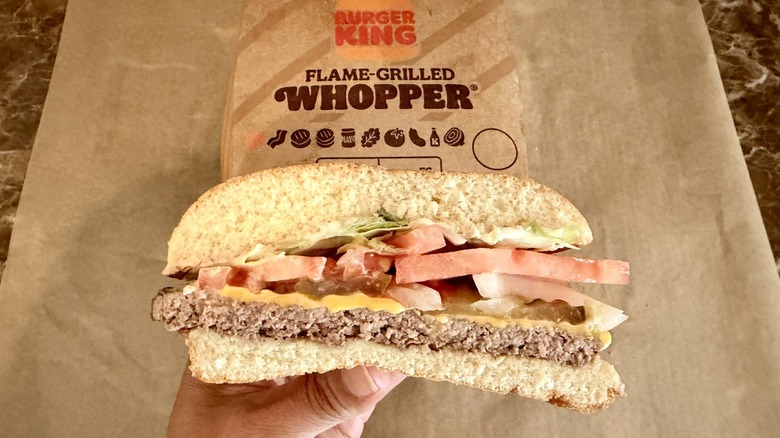 hand holding a half of a Whopper with packaging in the background