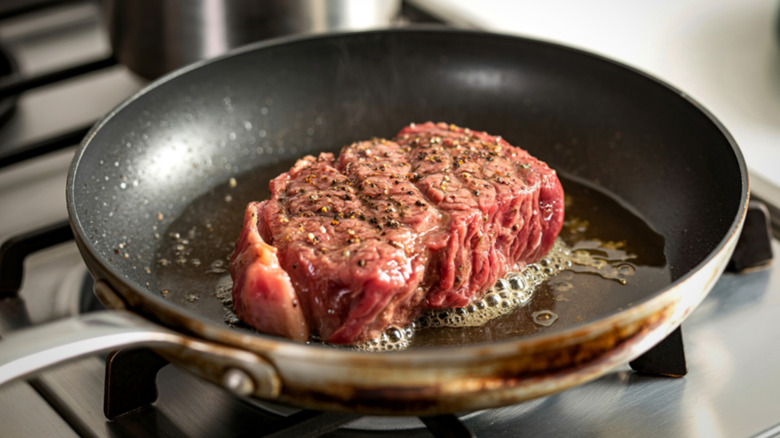 Steak cooking in oiled pan.