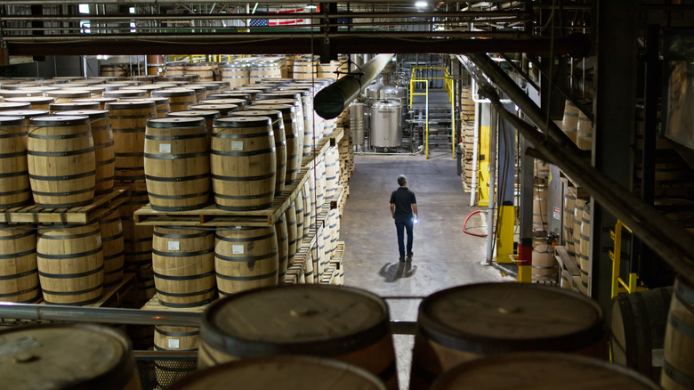 Person walking through warehouse full of whiskey barrels.