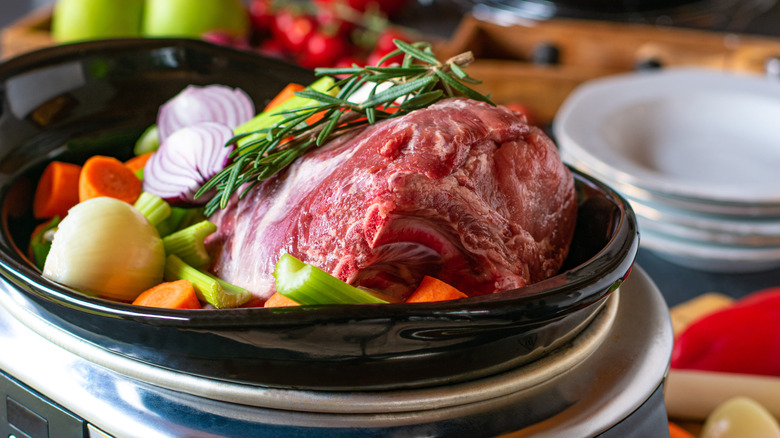 raw meat, vegetables, and fresh herbs in a slow cooker