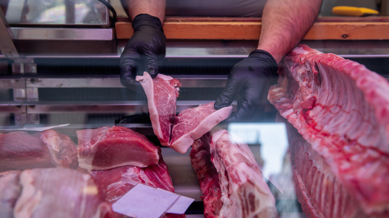 A butcher with gloved hands places steaks in a display case