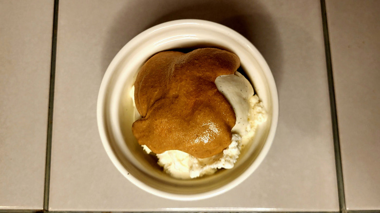Granola butter drizzled over vanilla ice cream in a small bowl.