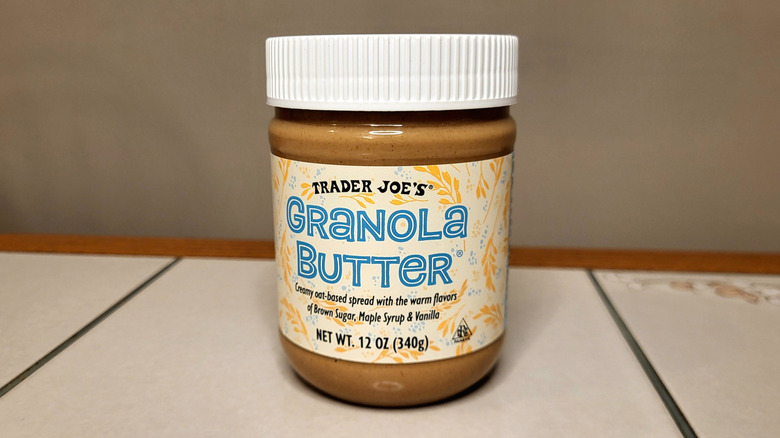 A jar of light brown granola butter on a tile table. The label reads 
