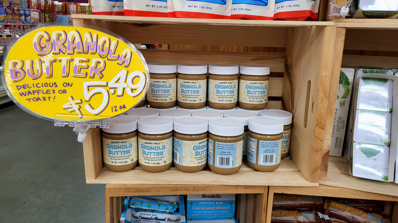 A granola butter display in a Trader Joe's store, showing several rows of the product in a wooden crate. The price is displayed on a yellow sign to the left.