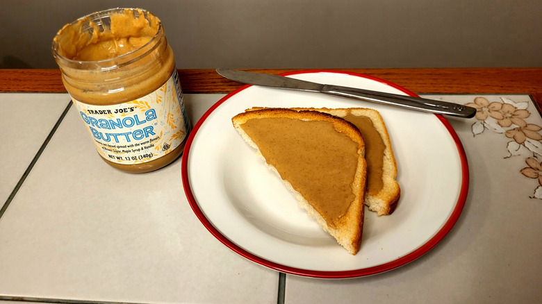 Granola butter spread onto a piece of toast on a plate sitting next to the jar.