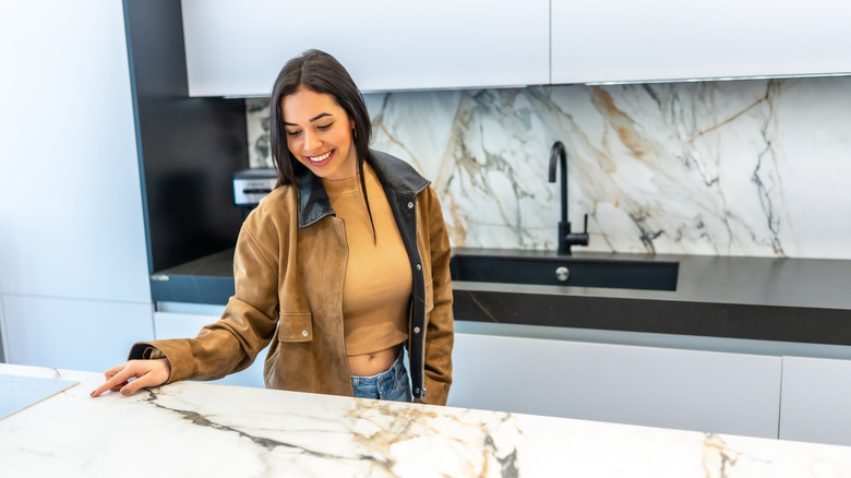 A woman admiring a veined marble countertop and matching backsplash.