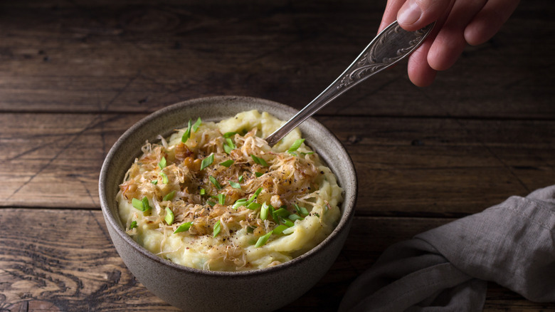 Hand stirring spoon in bowl of colcannon