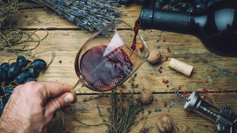 a galls of red wine being poured over a wooden table with herbs and spices on the background
