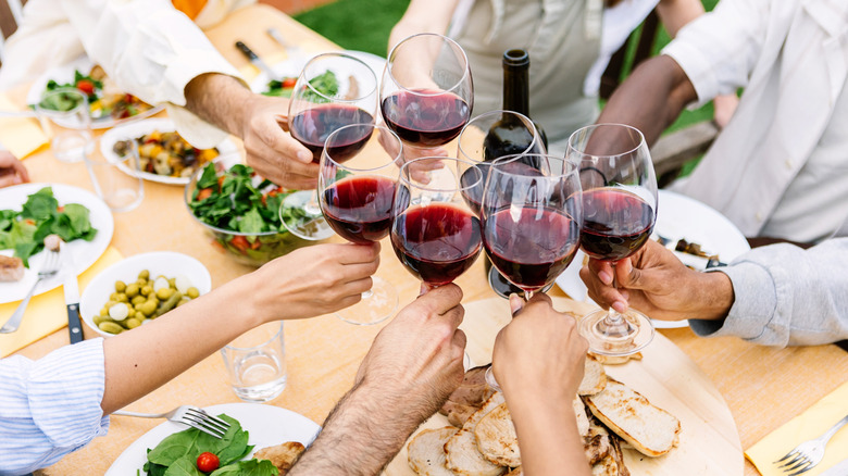 a group of friends eating outdoors and toasting with glasses of red wine