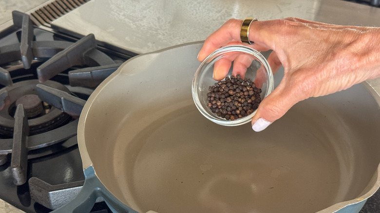 hand adding peppercorns to pan