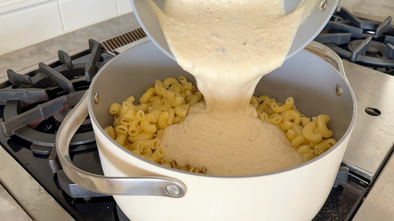 Pouring creamy sauce over elbow noodles in pot
