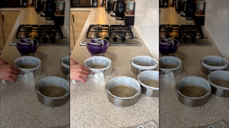 Cake tins sit on a kitchen counter wrapped in tinfoil filled with cake batter