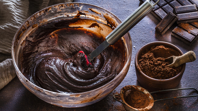 Closeup of brownie batter in a bowl on a table with cocoa powder and chocolate.