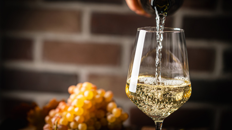 Sauvignon blanc wine being poured in a wine glass, with white grapes in the background