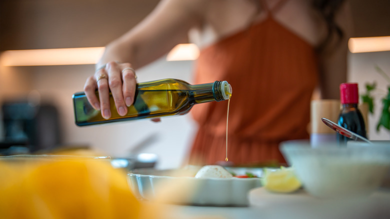 Person garnishing a dish with a glass bottle of olive oil.