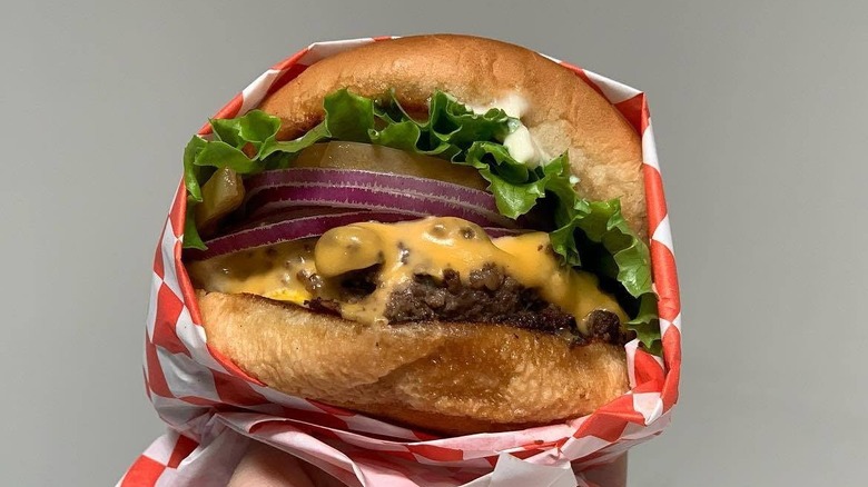 a burger wrapped in red-and-white-checked paper against a grey background