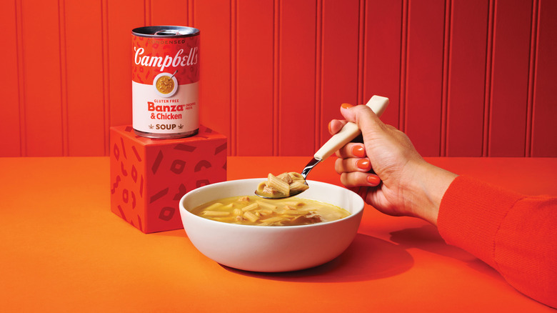 person spooning into Campbell's Condensed Banza Chickpea Pasta and Chicken Soup served in a white bowl