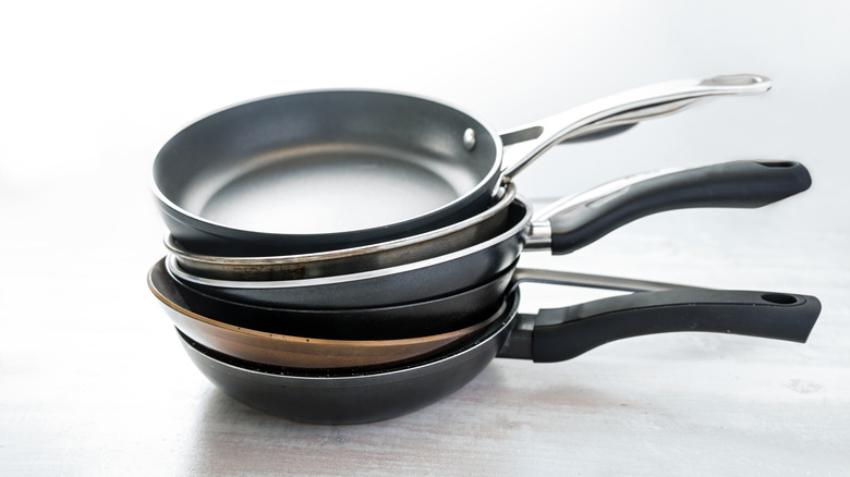 A stack of different types of skillets with metal and plastic handles