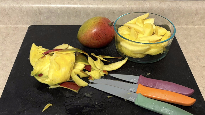 Slices of mango and knives on a black cutting board.
