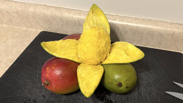 A peeled mango with other mangoes on a black cutting board.