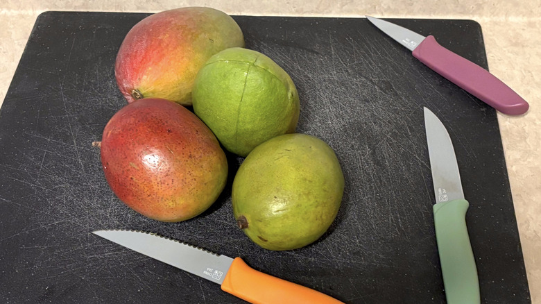 Mangoes on a black cutting board with assorted knives.